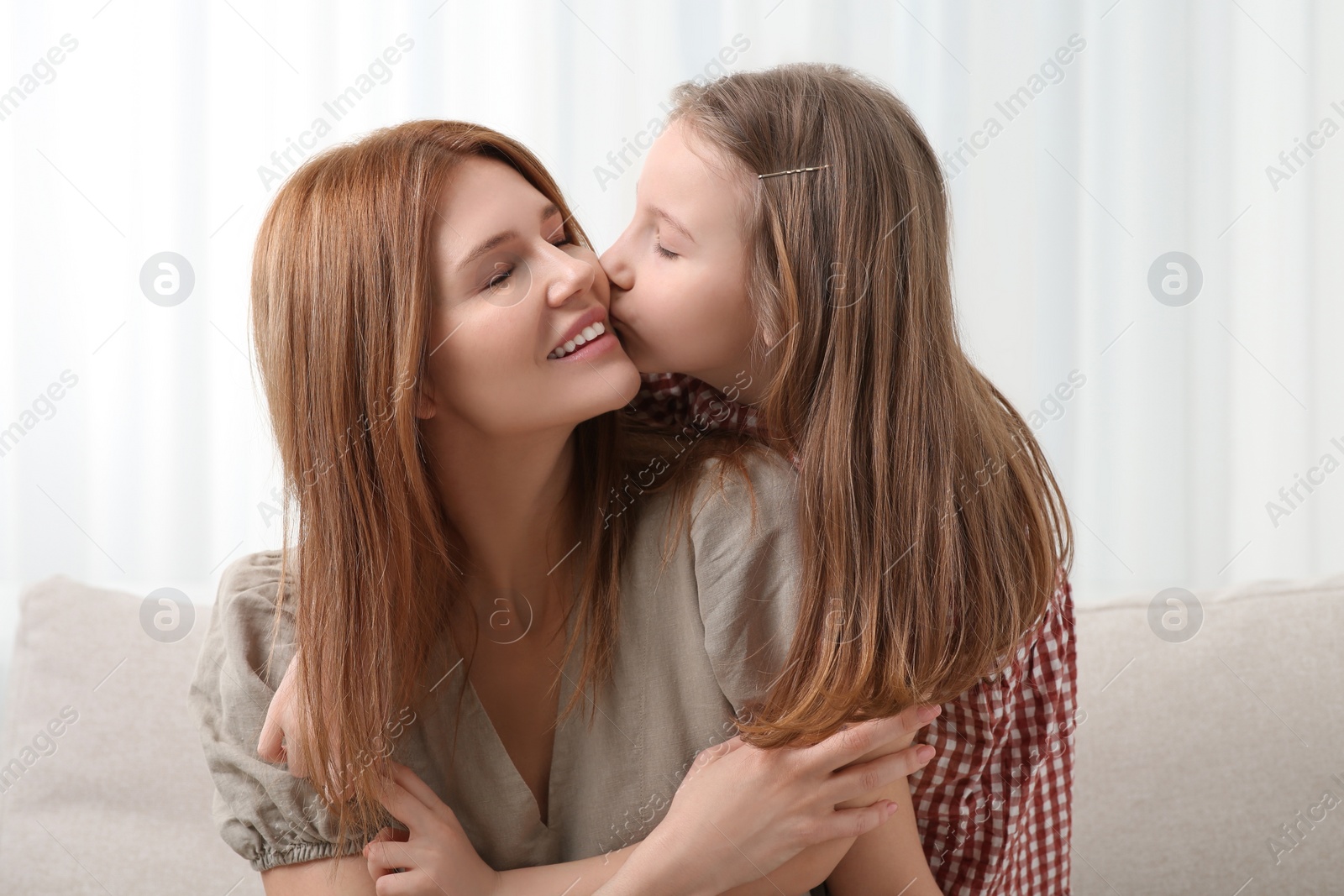 Photo of Cute daughter kissing her mom on sofa at home