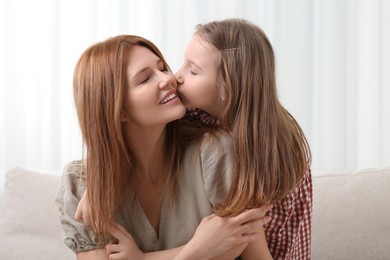 Cute daughter kissing her mom on sofa at home