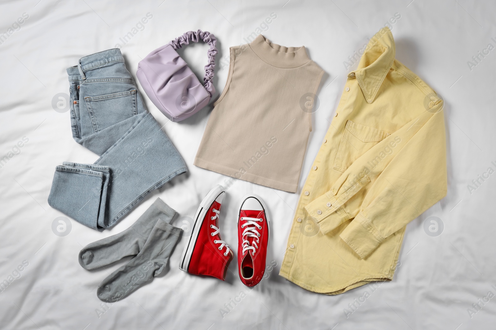 Photo of Pair of stylish red sneakers, clothes and bag on white fabric, flat lay