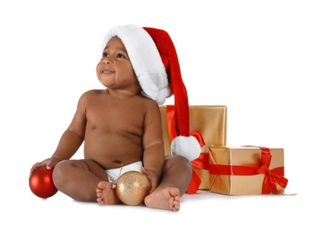Cute African-American baby wearing Santa hat with Christmas gifts on white background