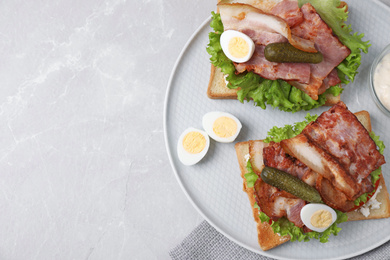 Tasty sandwiches with bacon and quail eggs served on light grey table, top view