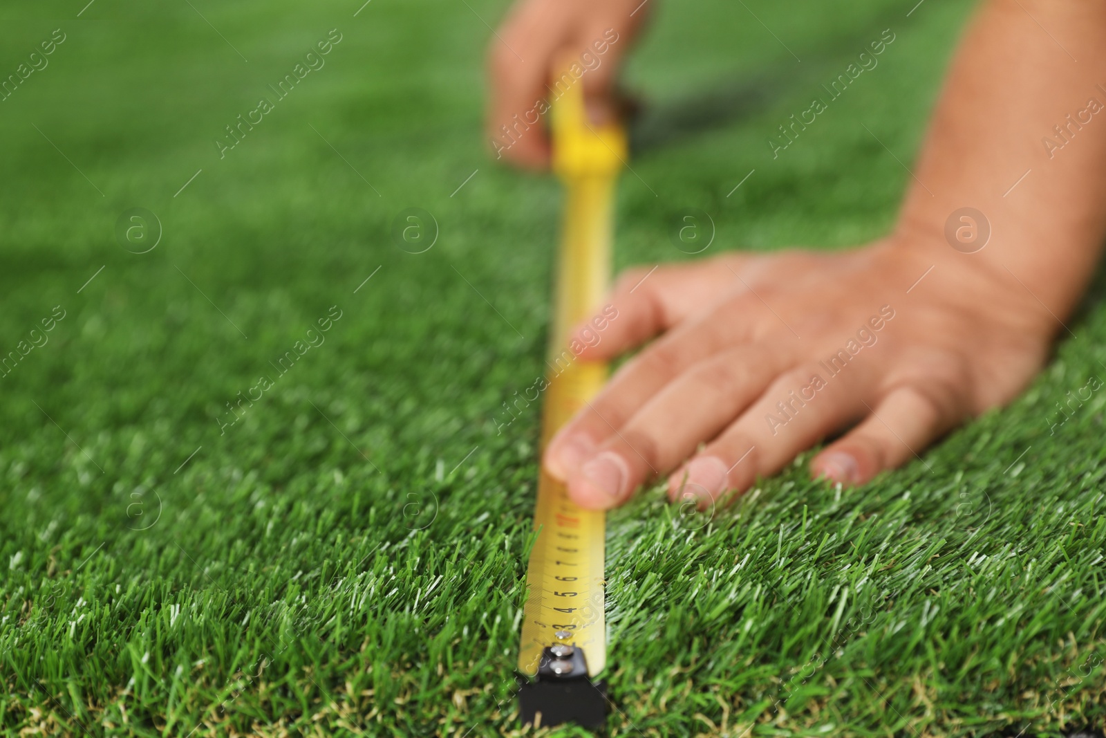 Photo of Man measuring artificial grass carpet indoors, closeup