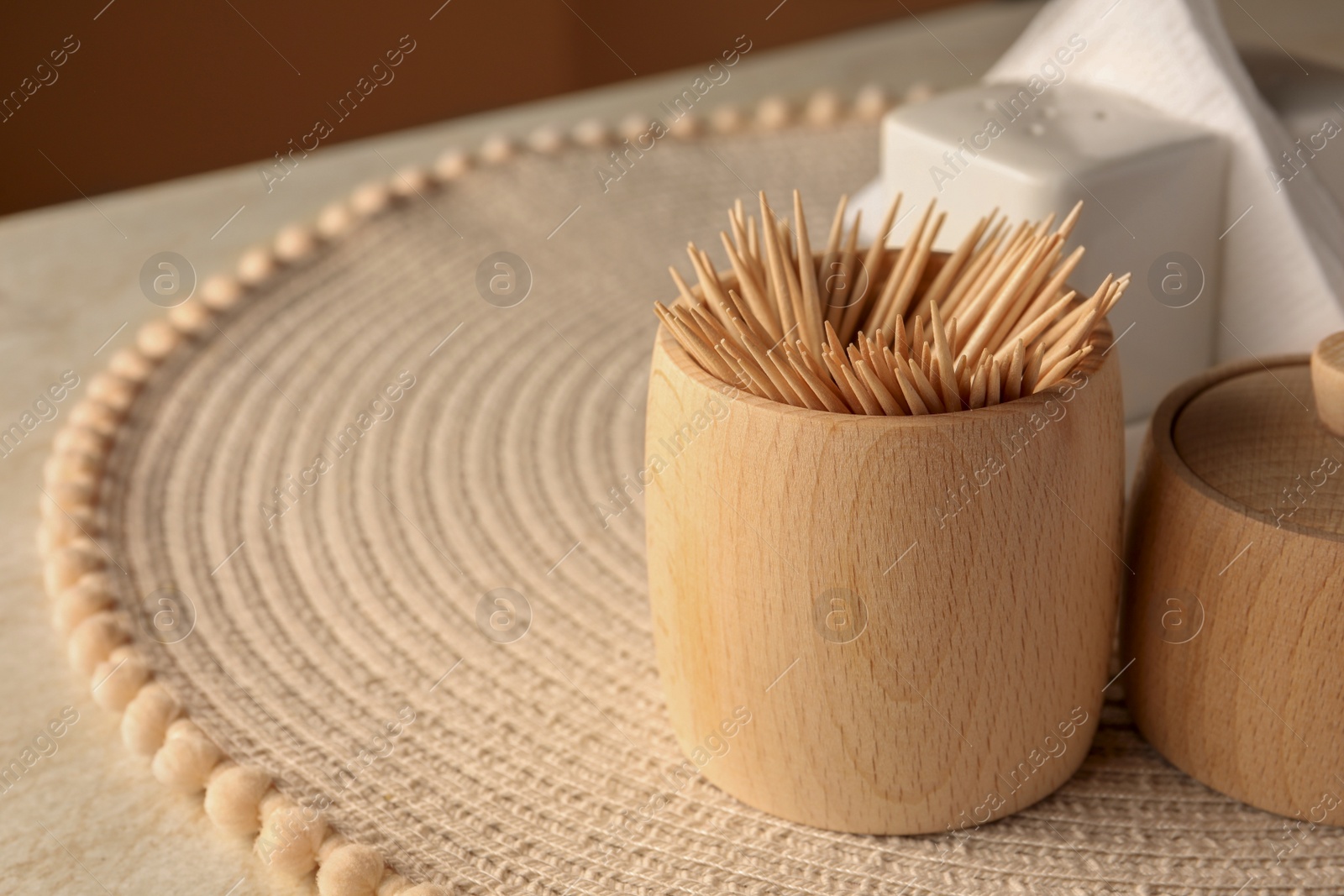 Photo of Wooden holder with many toothpicks on wicker mat, closeup. Space for text