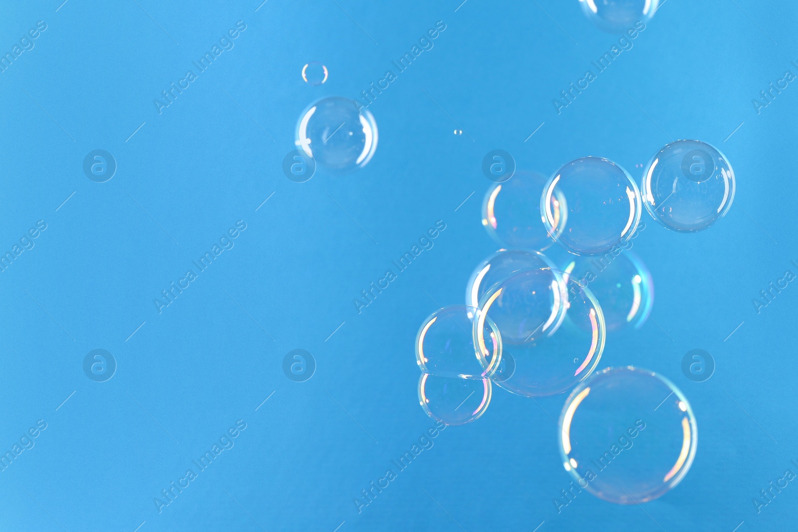 Photo of Beautiful transparent soap bubbles on light blue background, space for text