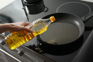 Photo of Woman pouring cooking oil from bottle into frying pan, closeup