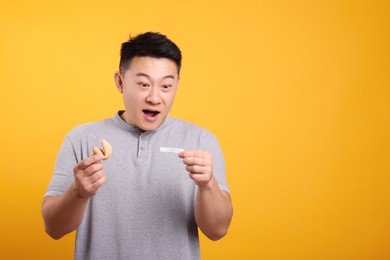 Photo of Emotional asian man holding tasty fortune cookie and reading prediction on orange background. Space for text