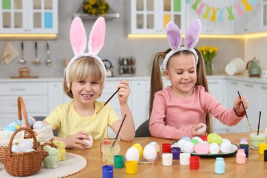 Photo of Children painting Easter eggs at table in kitchen