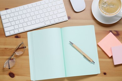 Photo of Empty notebook, keyboard, coffee and stationery on wooden table, flat lay