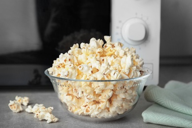 Photo of Glass bowl with tasty popcorn on table in kitchen