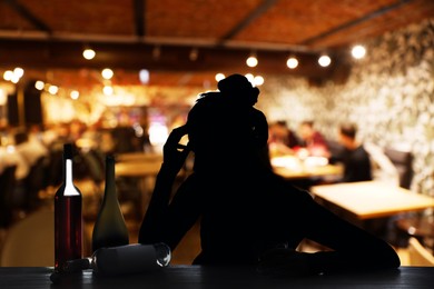 Image of Alcohol addiction. Silhouette of woman with glass and bottles in bar