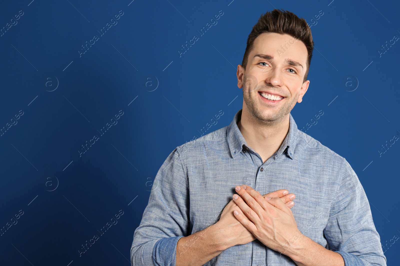 Photo of Handsome grateful man with hands on chest against blue background