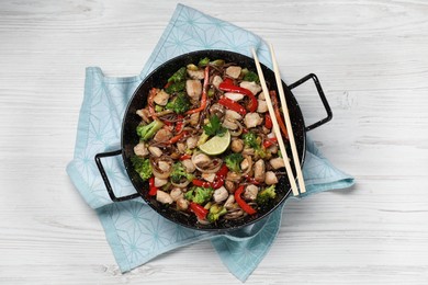 Photo of Stir-fry. Tasty noodles with meat in wok and chopsticks on white wooden table, top view