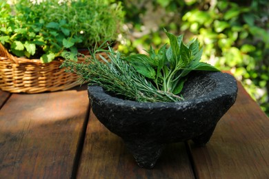 Photo of Mortar with thyme, rosemary and basil on wooden table outdoors, space for text. Aromatic herbs