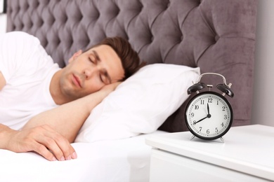 Photo of Young man sleeping in bed and alarm clock on nightstand at home