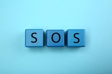 Photo of Abbreviation SOS (Save Our Souls) made of cubes with letters on light blue background, top view