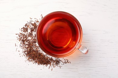 Photo of Freshly brewed rooibos tea and scattered dry leaves on white wooden table, flat lay