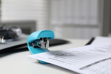 Photo of Stapler with document on white table indoors, closeup