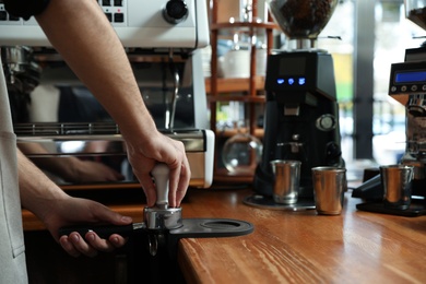 Photo of Barista tamping coffee in portafilter at bar counter, closeup. Space for text