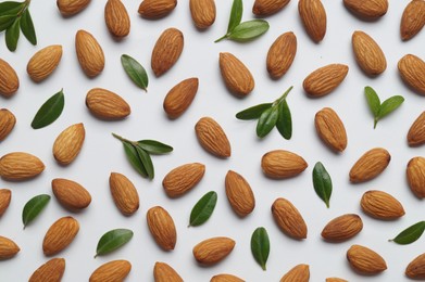 Photo of Delicious almonds and fresh leaves on white background, flat lay