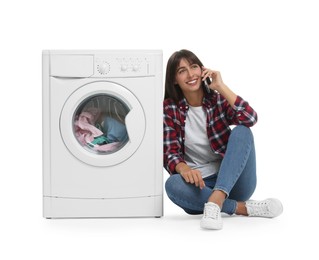 Beautiful woman talking on smartphone near washing machine with laundry against white background