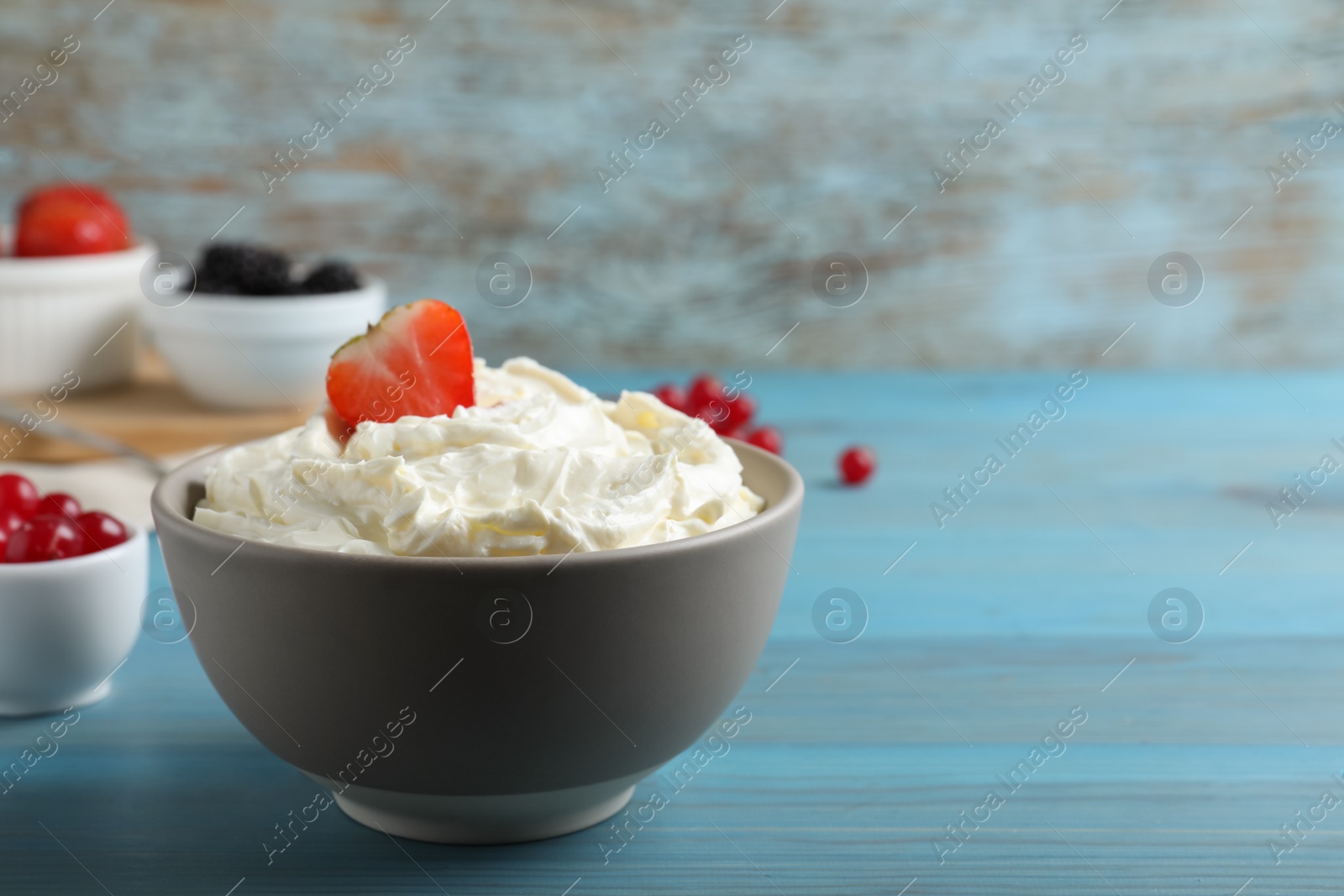 Photo of Tasty cream cheese and fresh berries on light blue wooden table. Space for text