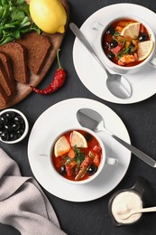 Meat solyanka soup with sausages, olives and vegetables served on dark grey textured table, flat lay