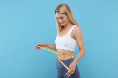 Photo of Slim woman measuring waist with tape on light blue background. Weight loss