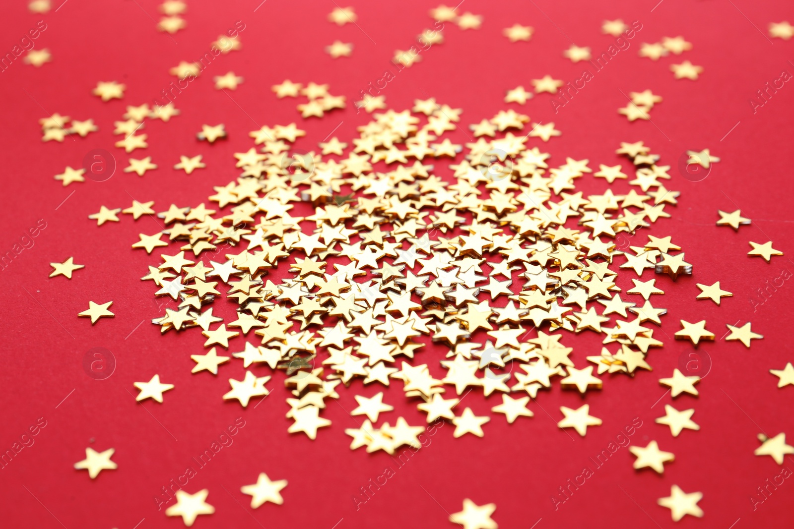 Photo of Gold confetti stars on red background, closeup. Christmas celebration