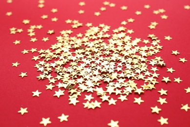 Gold confetti stars on red background, closeup. Christmas celebration