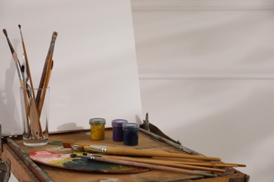 Photo of Easel with blank canvas, palette and brushes in art studio. Space for text