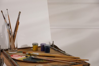 Easel with blank canvas, palette and brushes in art studio. Space for text