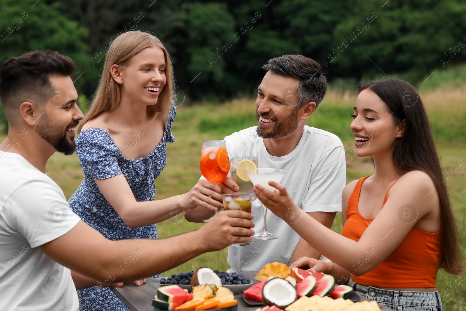 Photo of Happy friends clinking glasses with cocktails at table outdoors