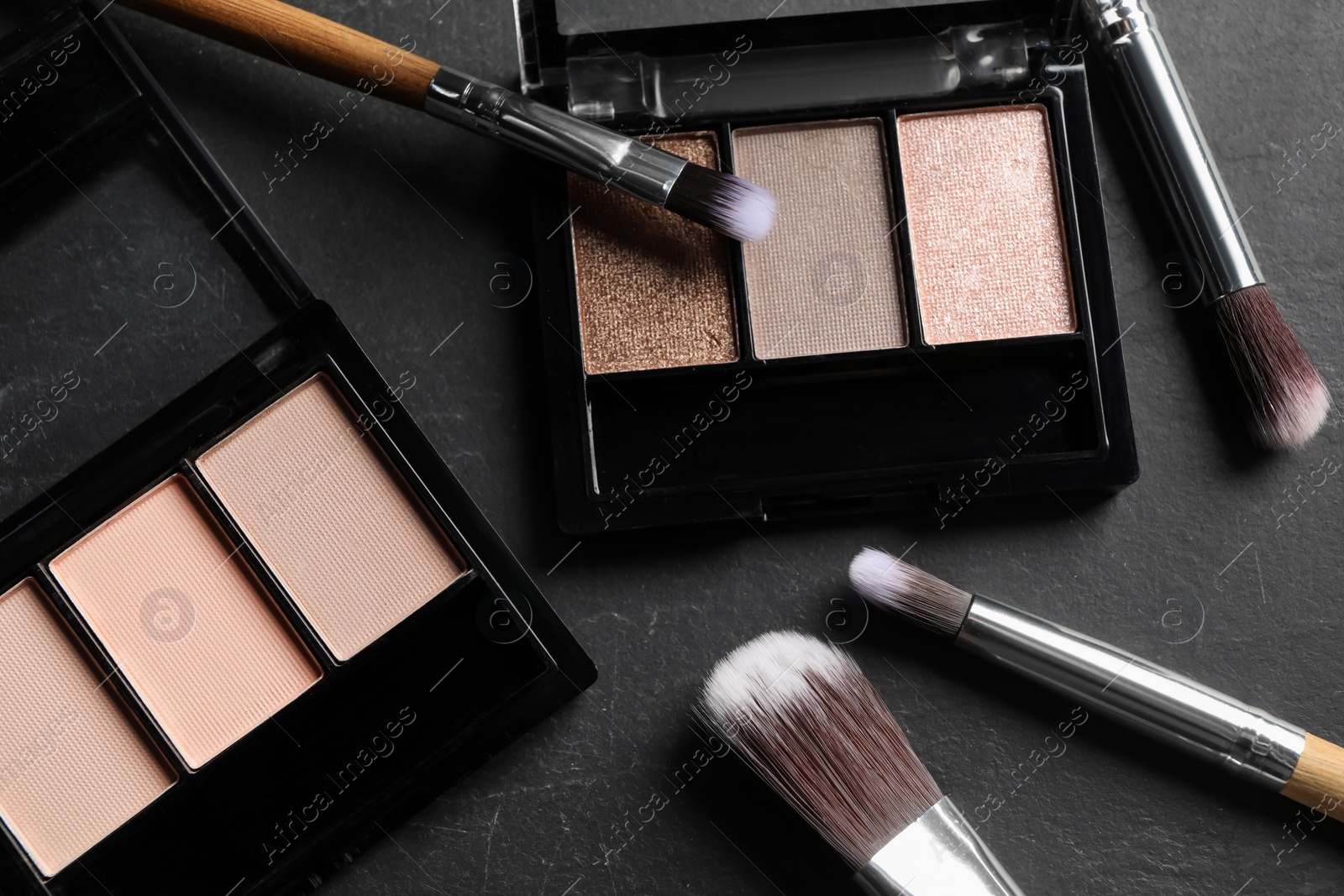 Photo of Beautiful eye shadow palettes and brushes on dark grey textured table, flat lay