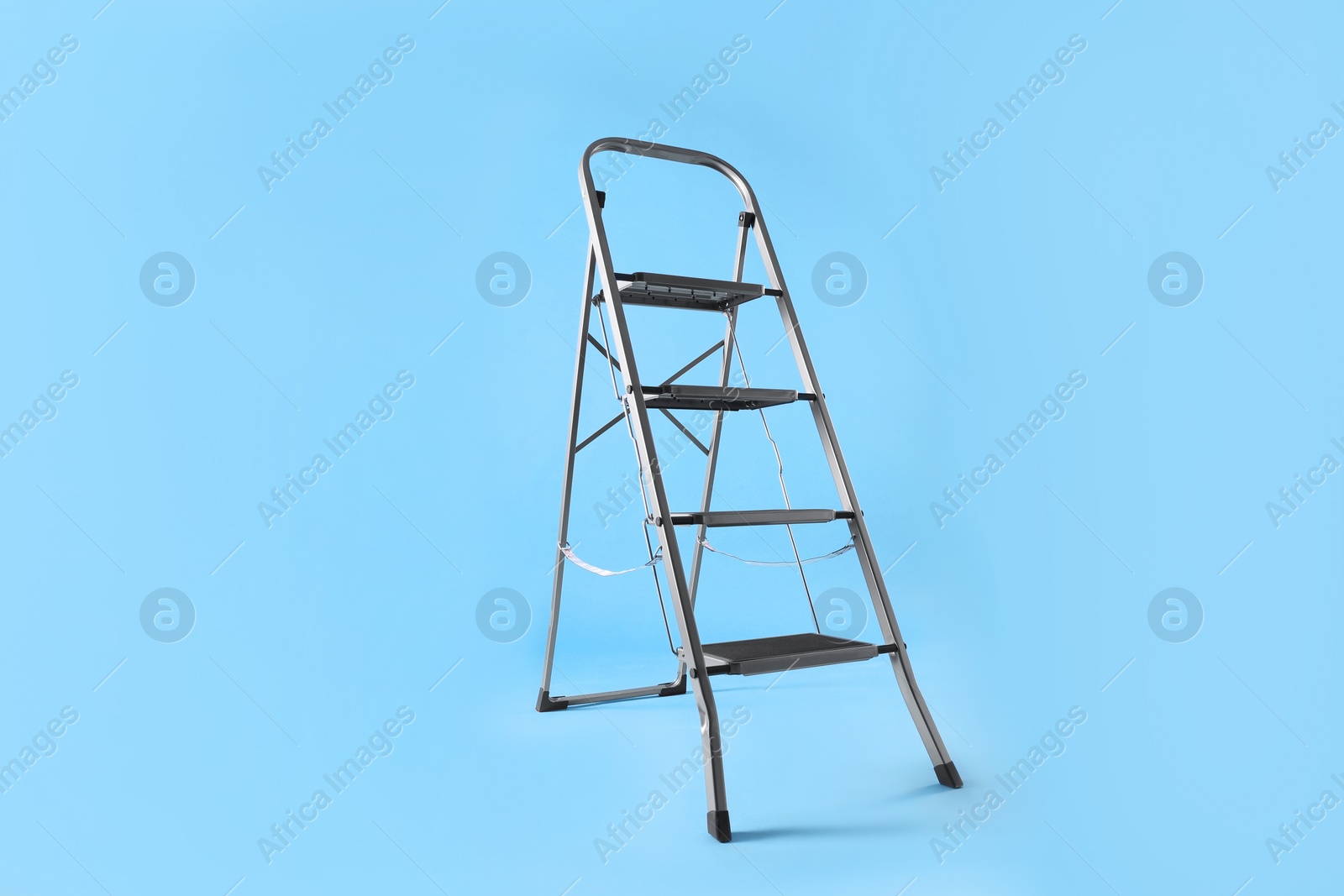 Photo of Metal stepladder on light blue background. Construction equipment