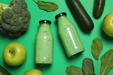 Photo of Bottles of delicious smoothie and ingredients on green background, flat lay