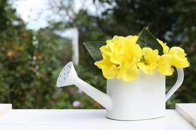 Photo of Watering can with beautiful yellow oenothera flowers on white wooden table outdoors