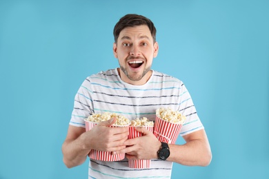 Emotional man with tasty popcorn on color background