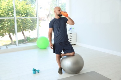 Tired overweight man drinking water in gym