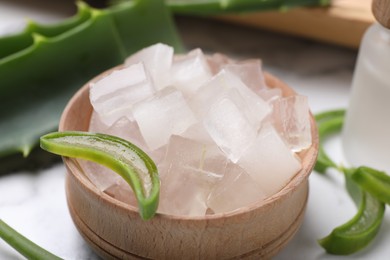 Photo of Aloe vera gel and slices of plant on white table, closeup