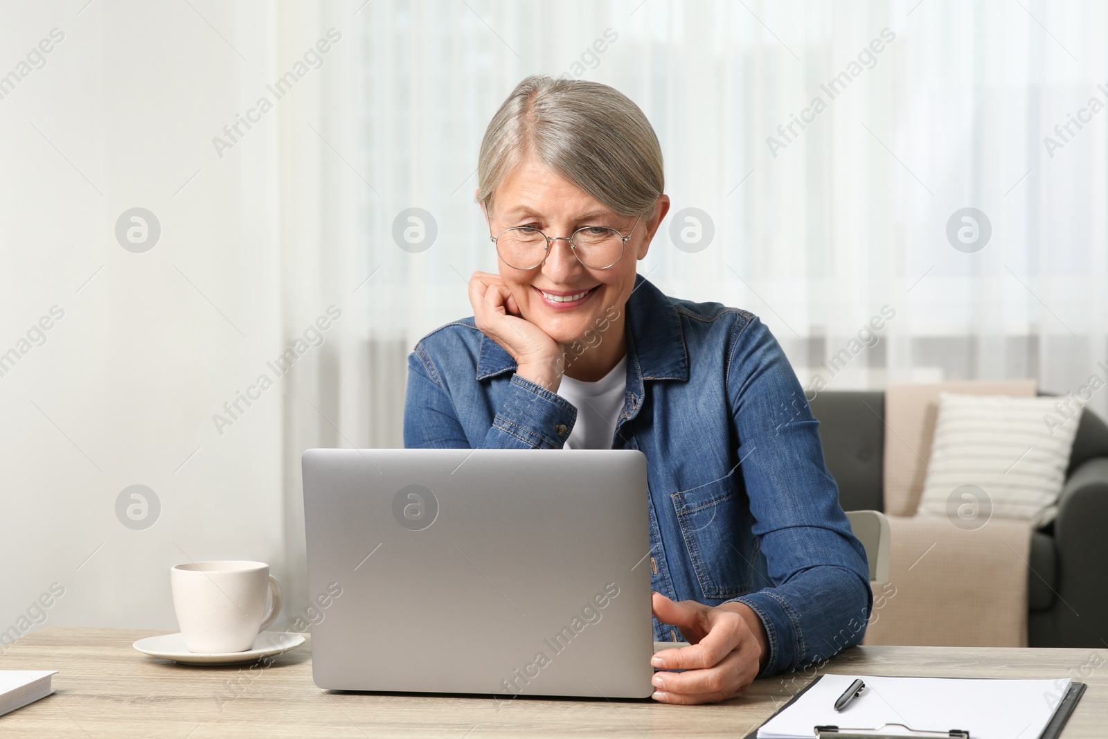 Photo of Beautiful senior woman using laptop at wooden table indoors