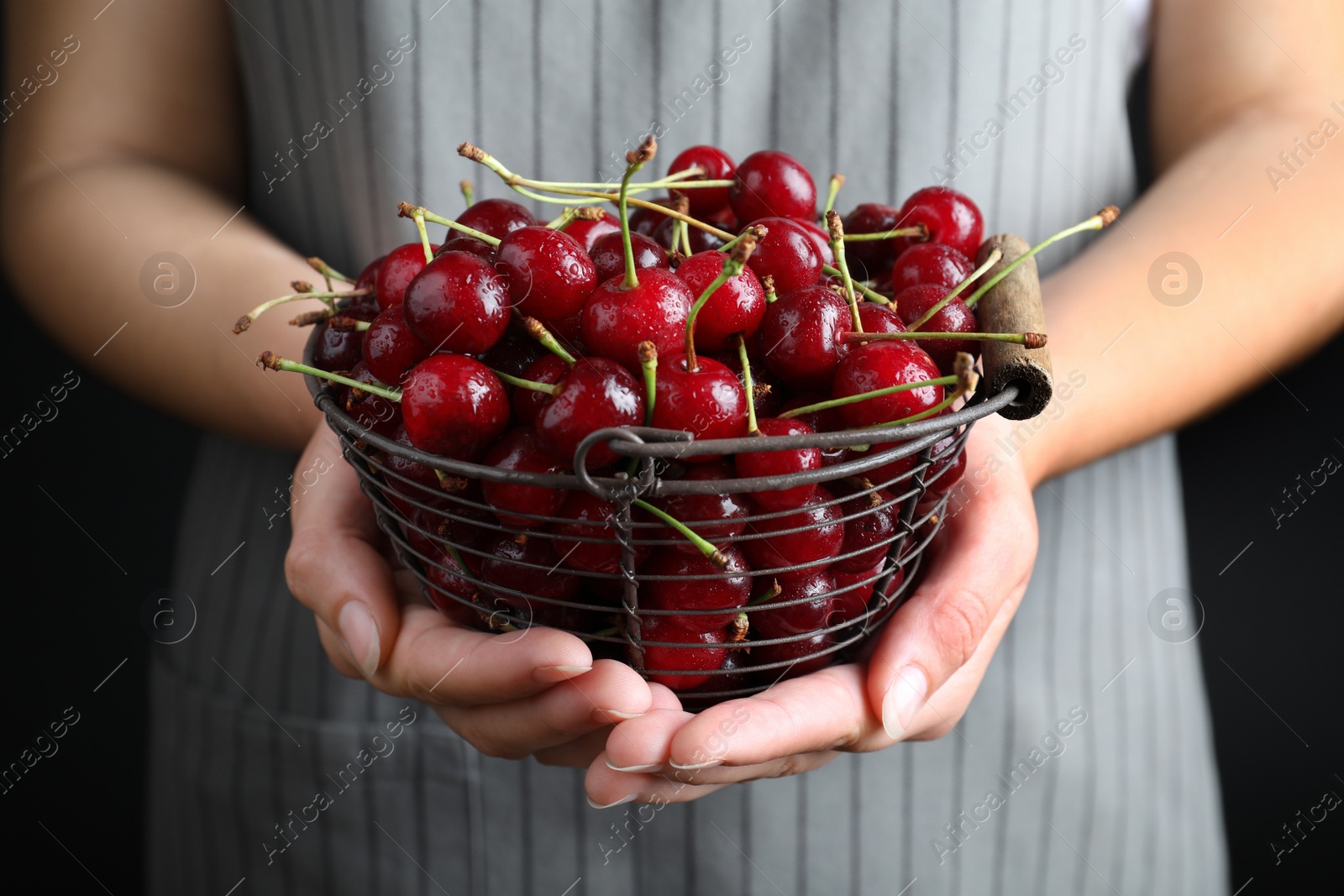 Photo of Woman holding metal basket with sweet juicy cherries on black background, closeup