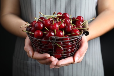 Photo of Woman holding metal basket with sweet juicy cherries on black background, closeup