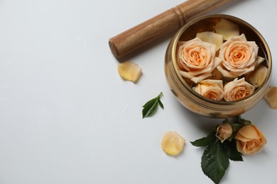 Tibetan singing bowl with water, mallet and beautiful rose flowers on white background, above view. Space for text