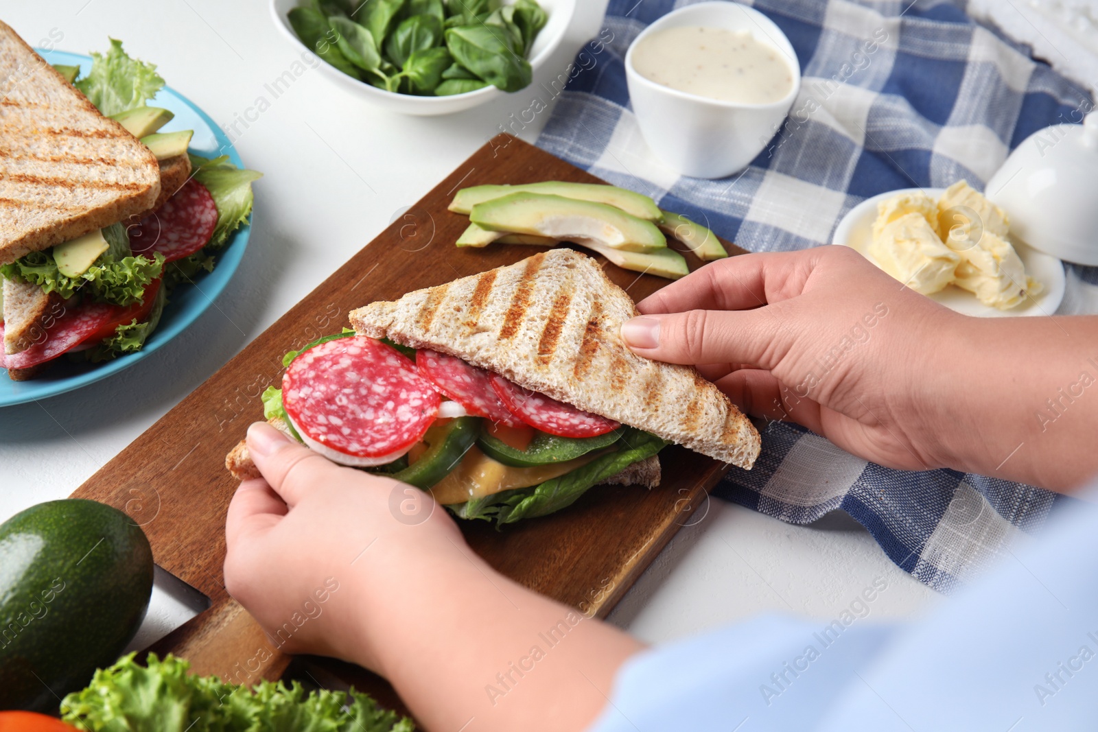 Photo of Woman making tasty sandwich with sausage at  white table, closeup