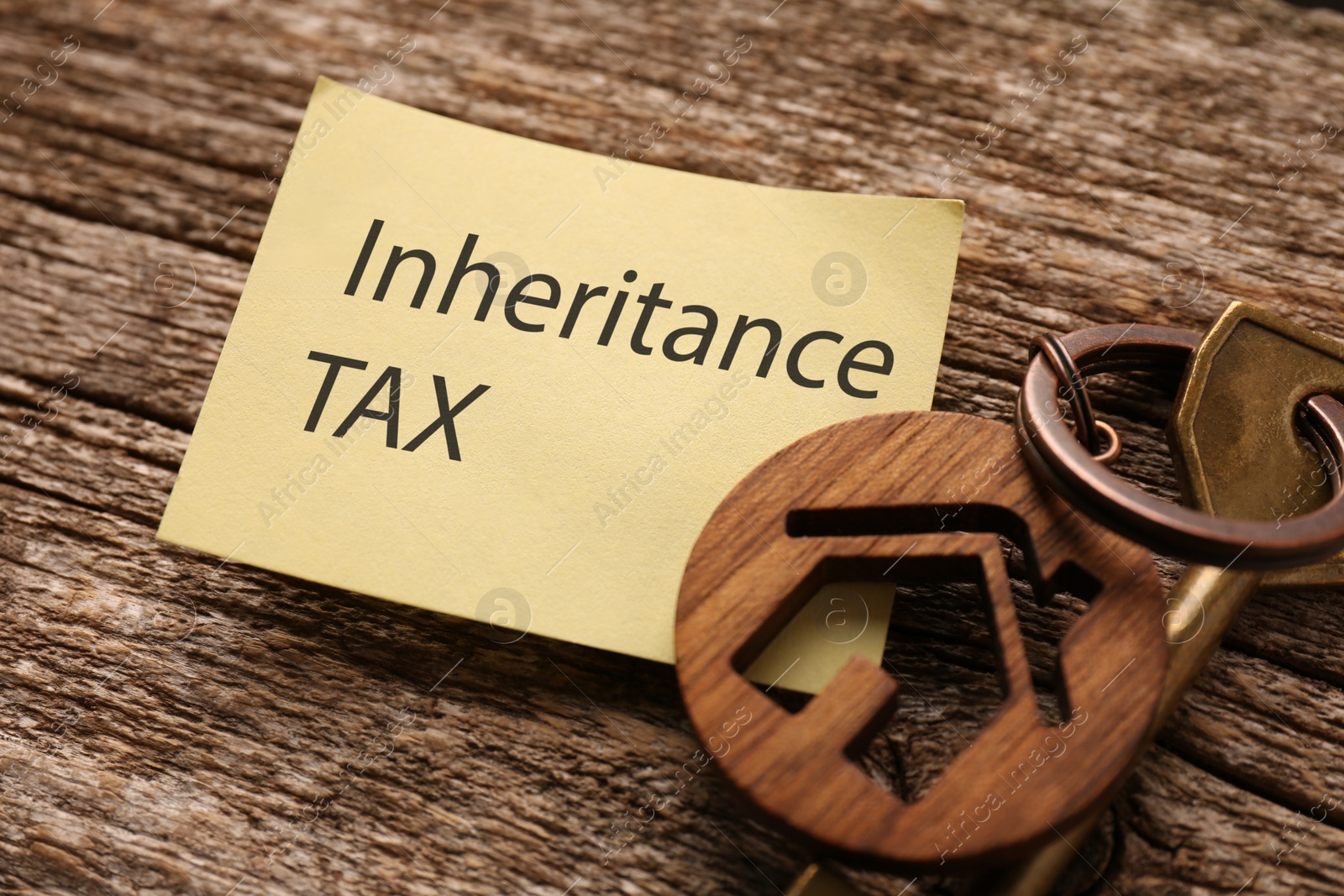 Photo of Inheritance Tax. Paper note and key with key chain in shape of house on wooden table, closeup