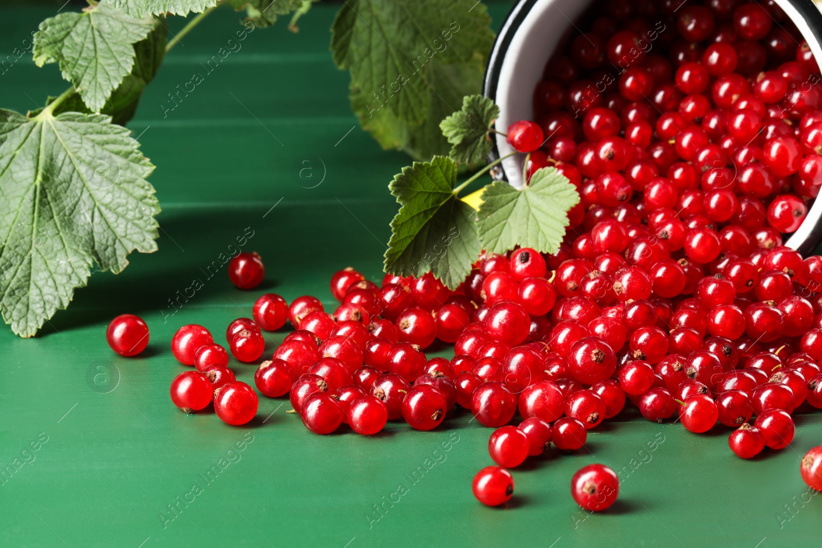 Photo of Many ripe red currants and leaves on green wooden table