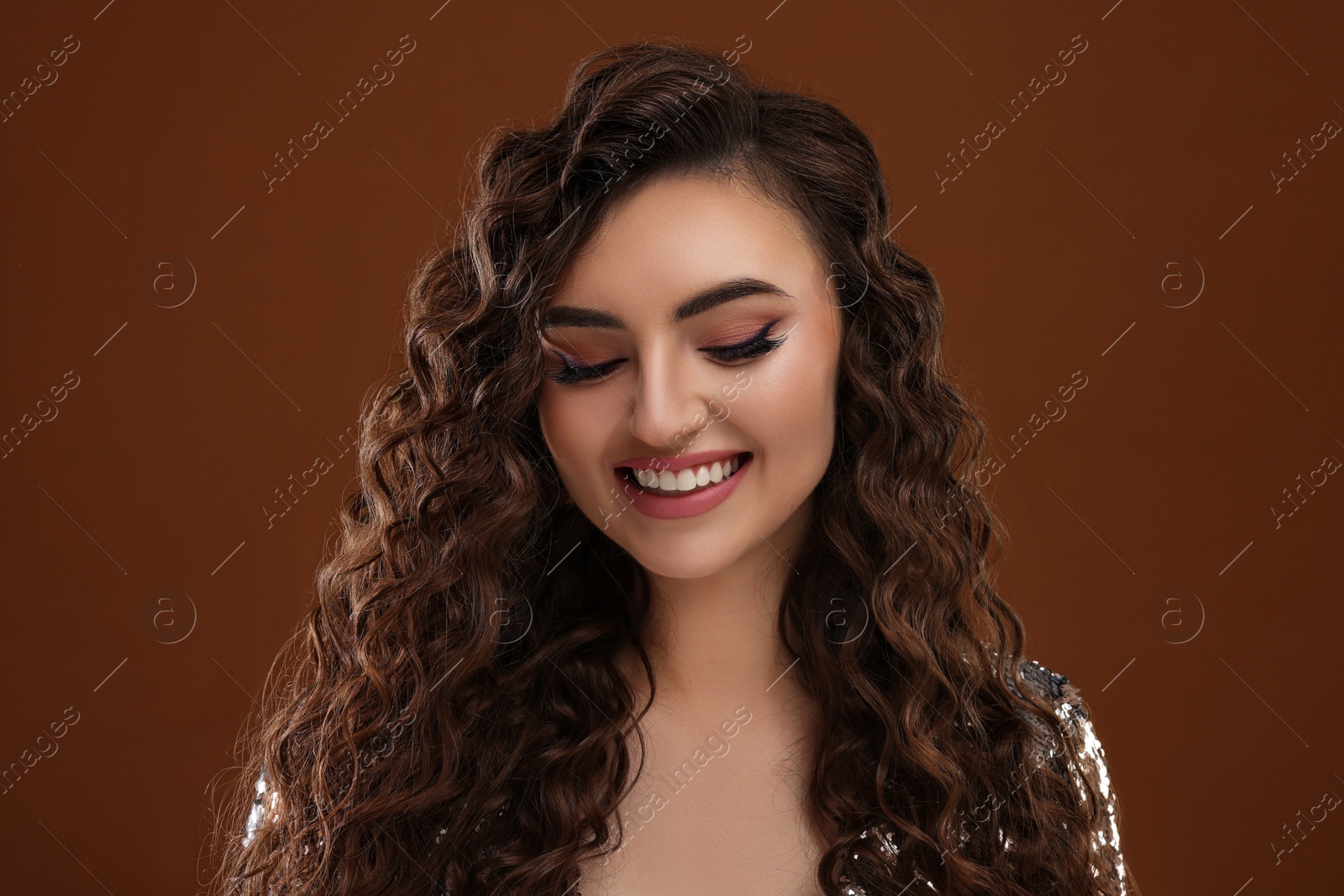 Photo of Beautiful young woman with long curly hair in sequin dress on brown background