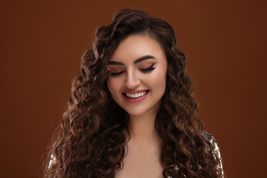 Beautiful young woman with long curly hair in sequin dress on brown background