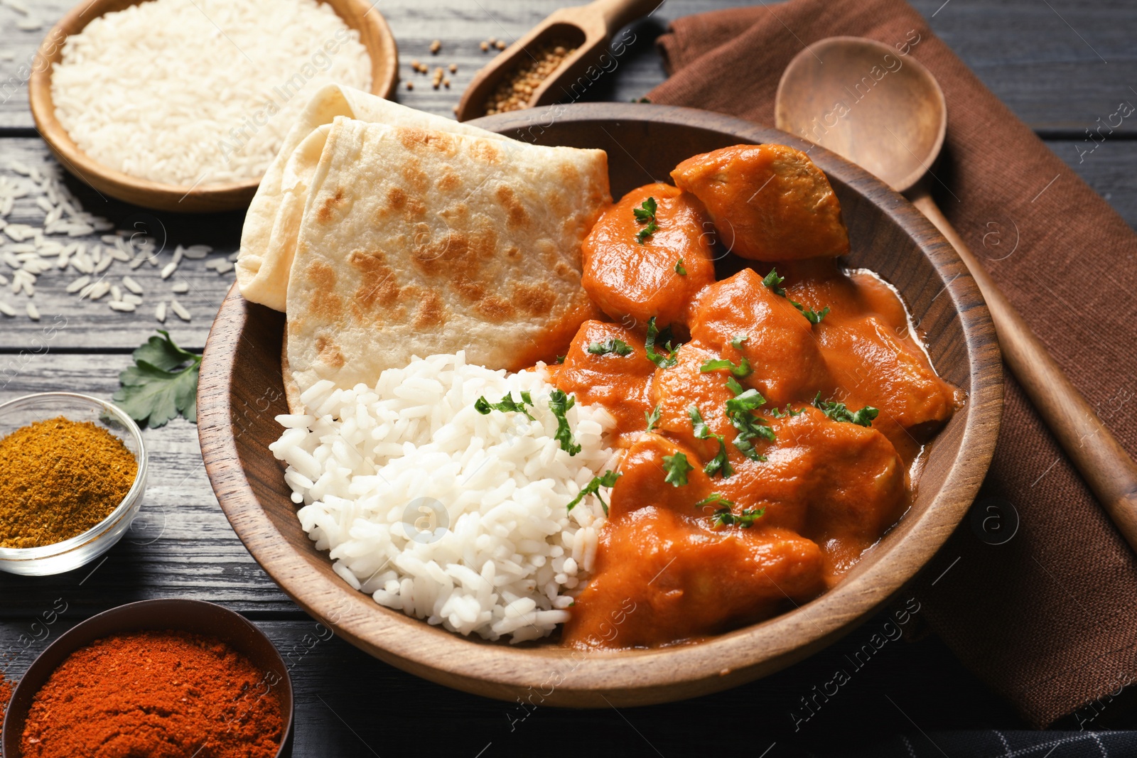 Photo of Delicious butter chicken with rice in bowl served on wooden table