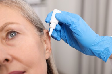 Photo of Medical drops. Doctor dripping medication into woman's ear indoors, closeup